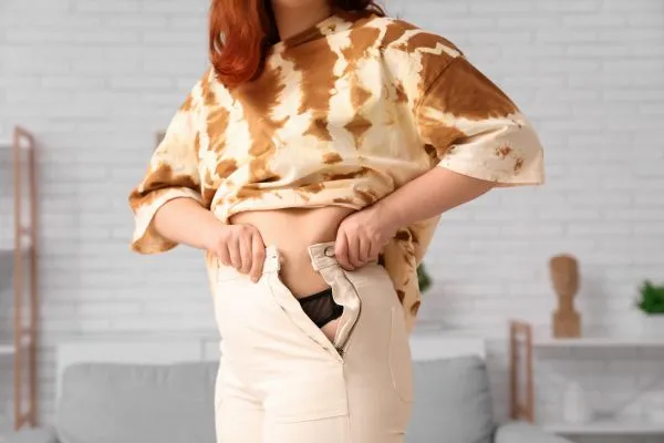 Image of woman trying to do her trousers up after pregnancy weight gain Kings Norton