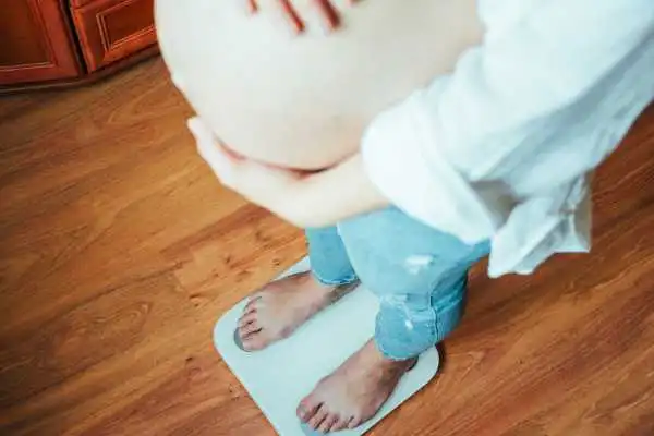 Image of woman weighing herself and experiencing weight gain through pregnancy Kings Norton